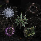 Glowing spider web stickers — white, green and violet — on a dark moody background