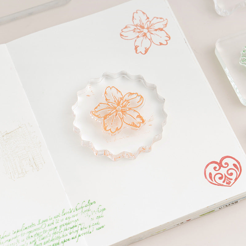 Clear acrylic stamp block pressing a floral stamp onto paper – transparent mounting plate for precise placement