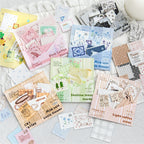 Display of all six styles of the vintage letterpress faux postage stamp ephemera packs, opened with their die-cut pieces beautifully spilling out. Showcases the variety of colors and themes available for junk journaling.