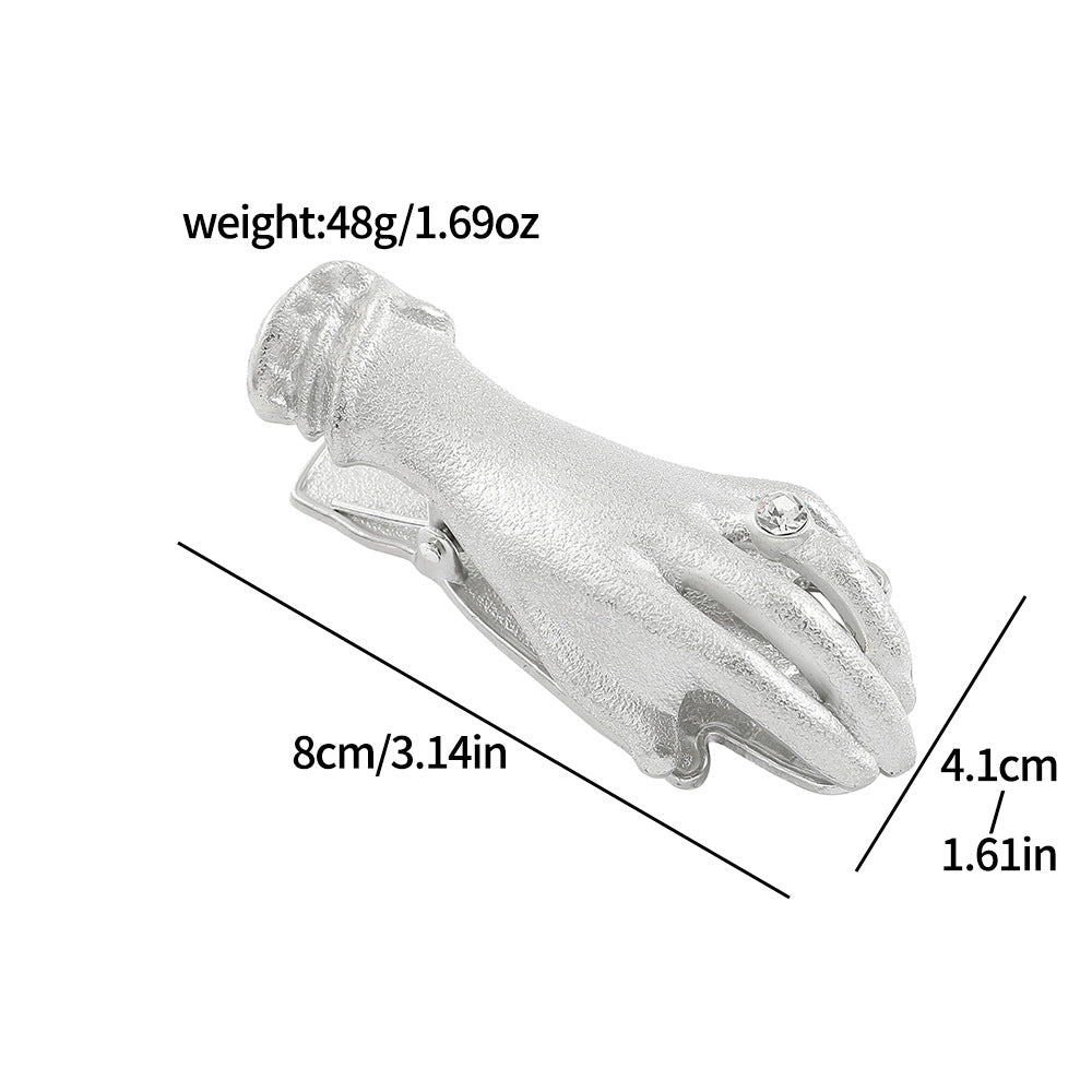 A large antique silver metal clamp shaped like a detailed hand holding large rose bouquets (no pearl detail). A visible rhinestone ring is on the finger. Ideal for taming stubborn pages in thick junk journals and gothic book accessories.