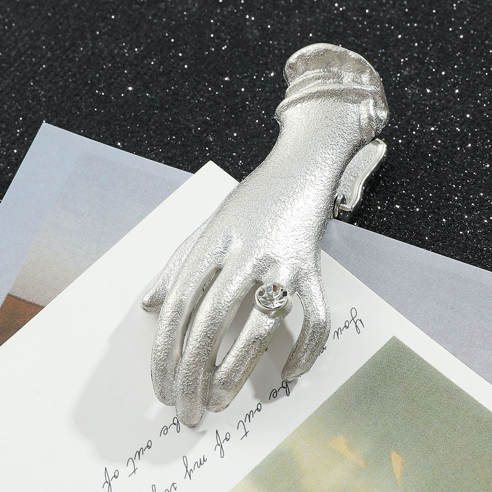 A delicate small antique silver metal journal clip in the shape of a Victorian lady's hand wearing a sparkling rhinestone ring. Resting on layered vintage cards, it is the perfect aesthetic paper holder and bookmark for vintage planners.