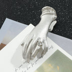 A delicate small antique silver metal journal clip in the shape of a Victorian lady's hand wearing a sparkling rhinestone ring. Resting on layered vintage cards, it is the perfect aesthetic paper holder and bookmark for vintage planners.