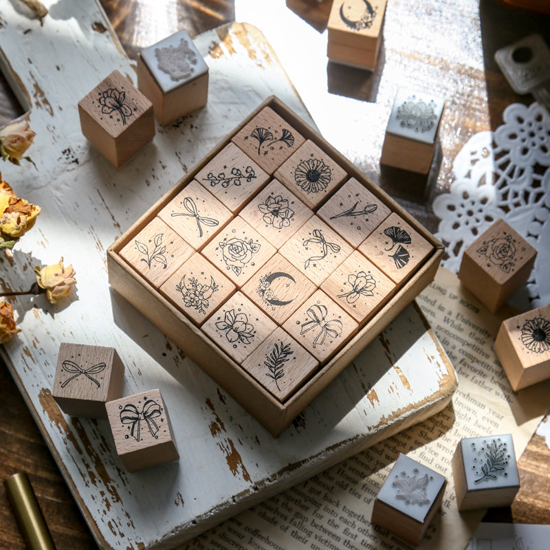 Top-down view of the 16-piece floral and botanical wooden stamp set neatly organized in a vintage kraft paper drawer box, surrounded by dried roses and sunlight.