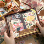 A detailed close-up showing the spine of the "Letter From Flowers" notebook and a roll of washi tape unrolled slightly to reveal its unique pattern of green botanical illustrations and vintage script text. Transparent sticker sheets are partially visible nearby.