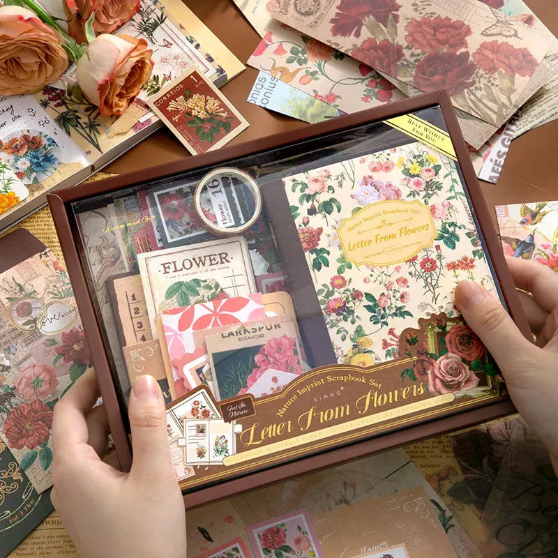 A detailed close-up showing the spine of the "Letter From Flowers" notebook and a roll of washi tape unrolled slightly to reveal its unique pattern of green botanical illustrations and vintage script text. Transparent sticker sheets are partially visible nearby.