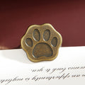 Antique bronze cat paw metal clip with vintage patina finish on dark red background