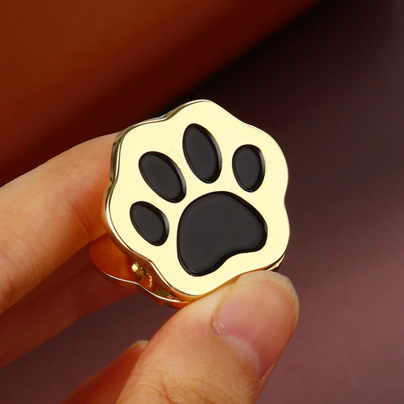 Hand holding gold cat paw metal clip with black toe pad showing compact size