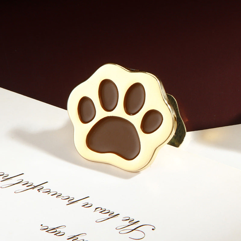 Gold cat paw metal clip with cocoa brown pad resting on white calligraphy paper