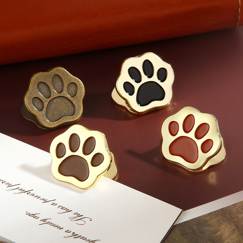 Four cat paw metal clips in black, cocoa, rust, and antique bronze on dark surface