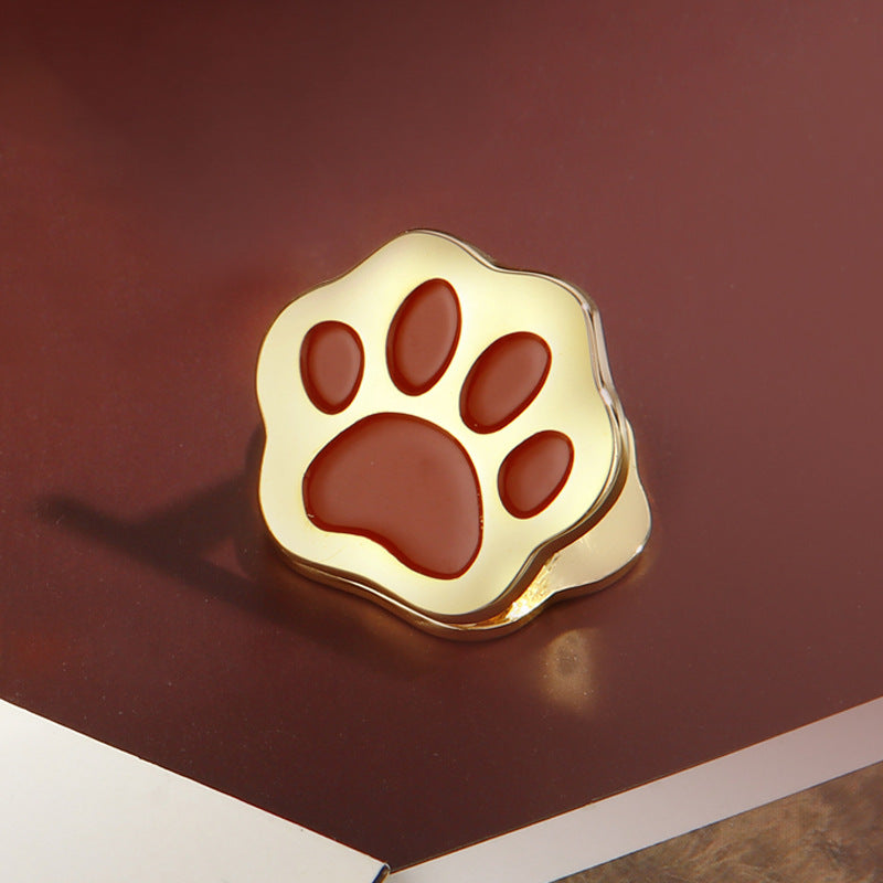 Gold cat paw metal clip with rust red pad on dark burgundy background