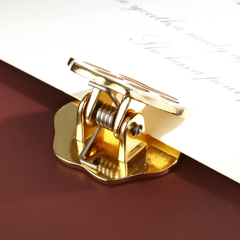 Metal spring clamp mechanism of cat paw journal clip gripping white paper securely