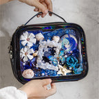 A person holding a black Ita bag decorated with the Celestial Ocean mixed media kit. The display window features an anime pin surrounded by blue mesh, white and blue 3D flowers, seashells, and a holographic butterfly.