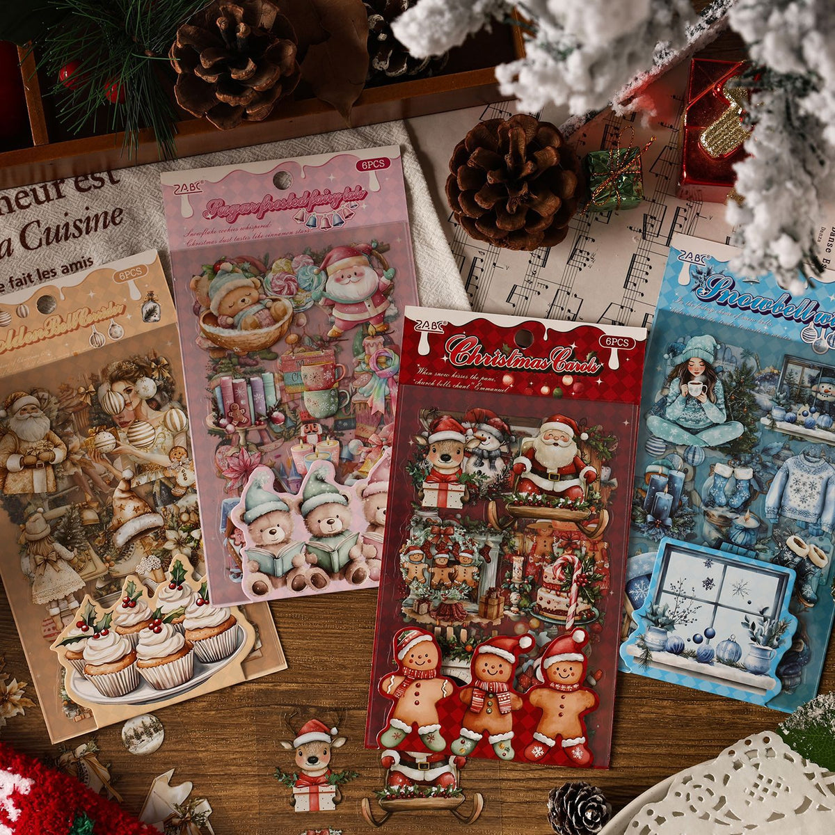 Four Christmas PET sticker packs arranged in a snowy scene with pine cones and fairy lights