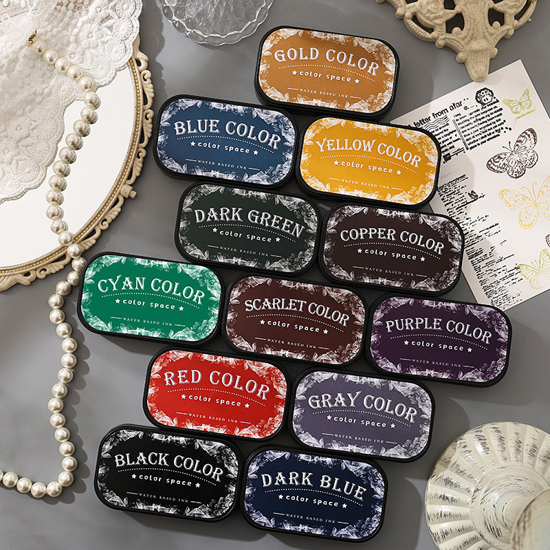 Twelve Color Space ink pads arranged on a gray desk with pearls and vintage ephemera