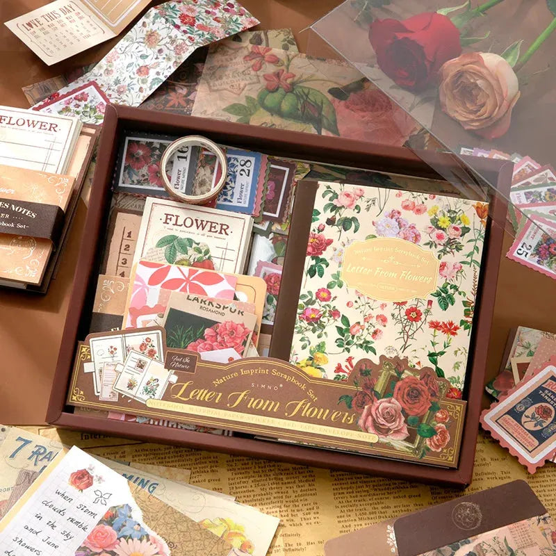 A beautiful flat lay showcasing the diverse contents of the "Letter From Flowers" scrapbooking kit. Features the floral notebook, translucent PET botanical stickers, washi sheets, ephemera papers with vintage script, and background decorative papers spread on a desk.
