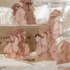 Macro shot of aesthetic girl silhouette PET stickers featuring soft pink outfits and pets. Layered against a rustic kraft box and knit blanket for cozy journaling inspiration.