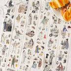 Opened box of the 'Cozy Café' washi tape set on a wooden table, next to a ceramic cup. The 6 rolls feature aesthetic illustrations of girls with coffee, fresh bread, and relaxing everyday life.