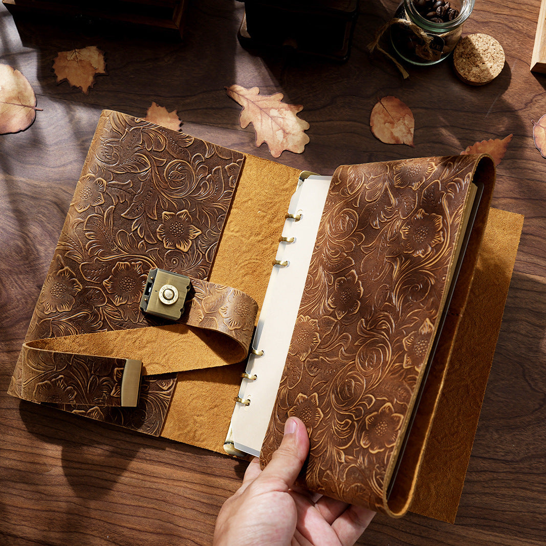 A hand opening the Embossed Antique Floral genuine crazy horse leather journal. Reveals the sturdy refillable 6-ring metal binder and thick blank ivory pages inside, highlighting the premium quality and functionality.
