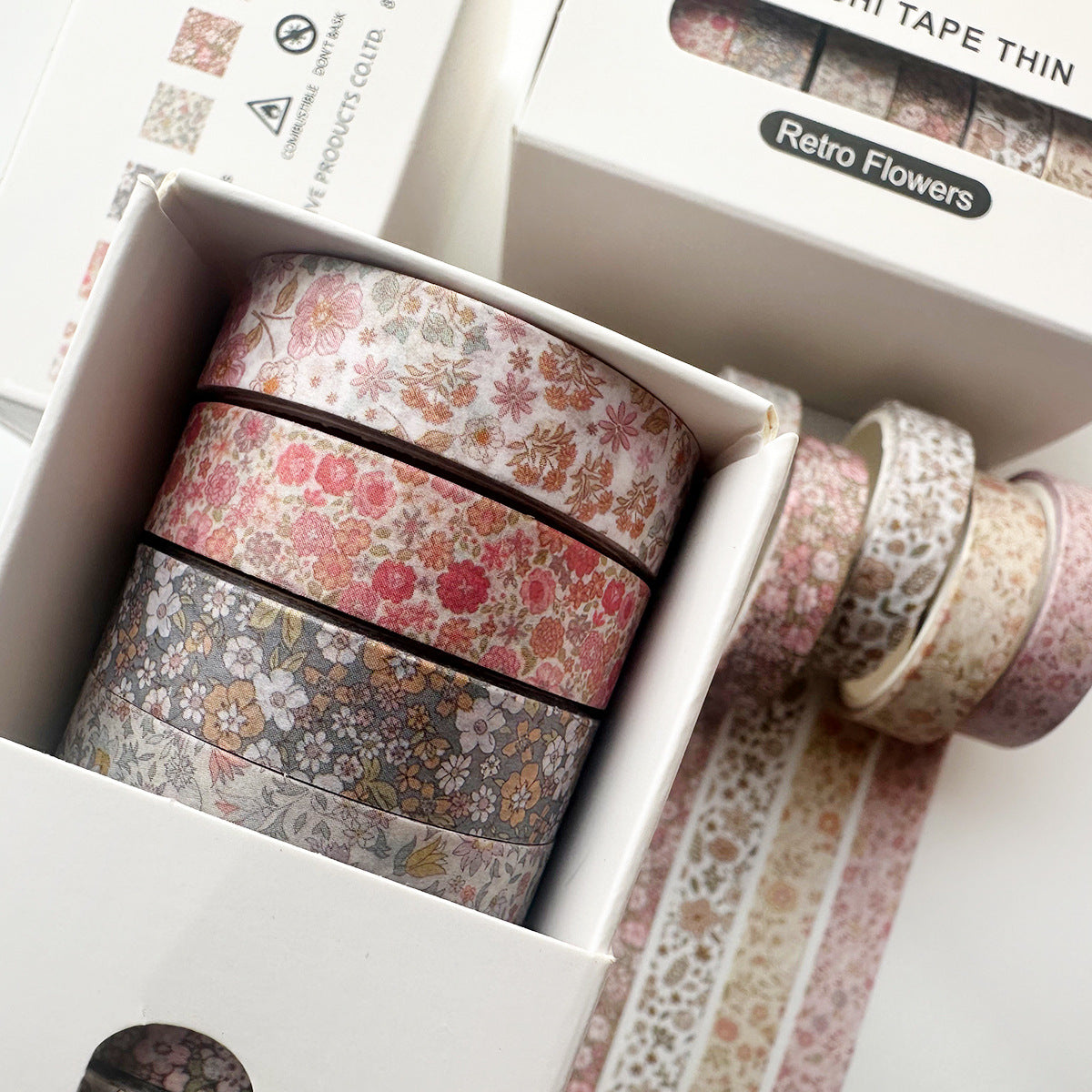 Close-up of the Faded Blossoms slim washi tape set partially inside its box, with unrolled strips revealing dusty pink botanical and floral designs for Cottagecore aesthetics.