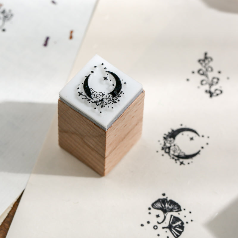 Macro shot of the floral moon wooden stamp resting on paper, showing crisp black ink impressions of the moon and ginkgo leaf designs for aesthetic bullet journaling.