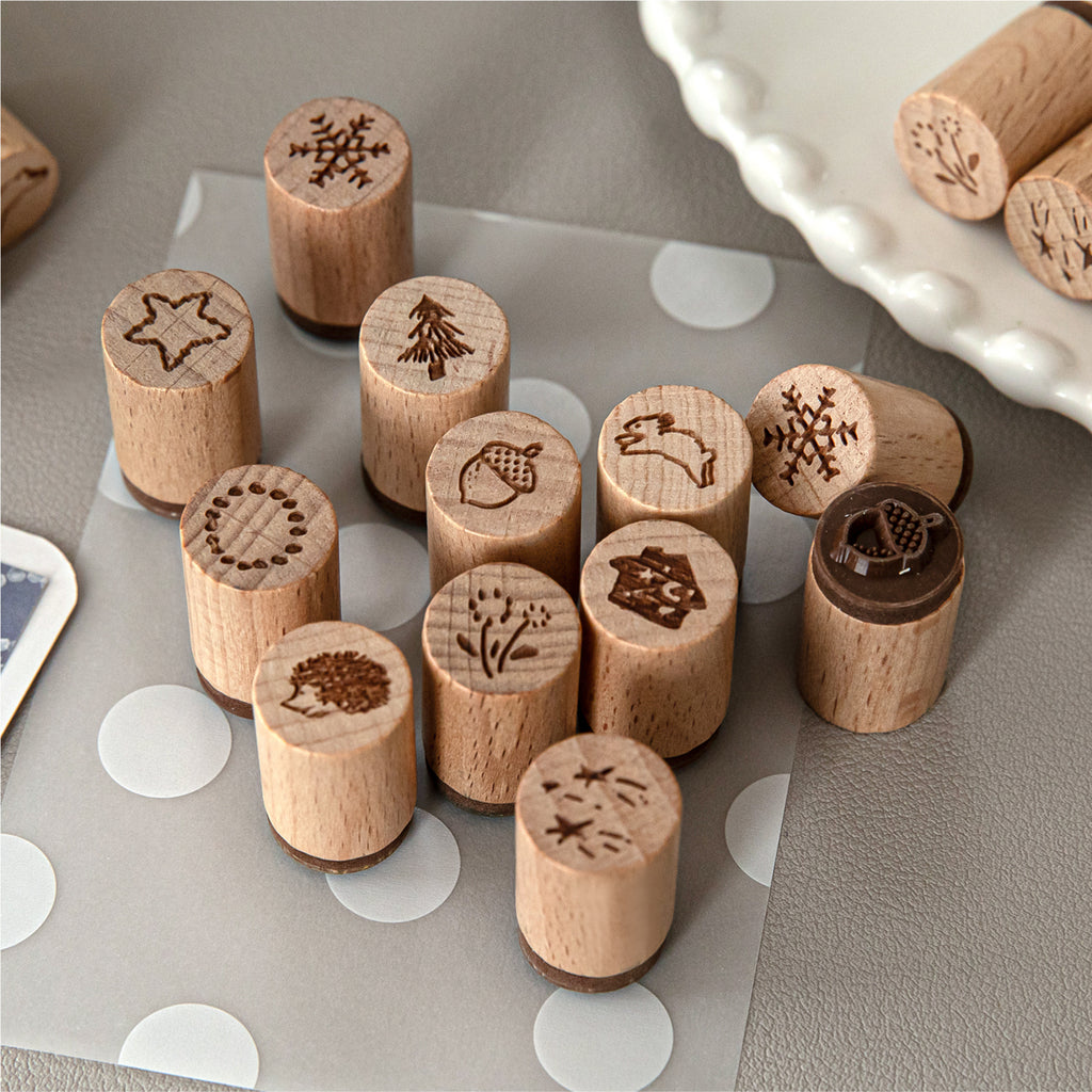 Hand-drawn forest wooden stamps scattered on grey desk, showing pine tree, star, snowflake, and cottage designs.