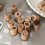 Hand-drawn forest wooden stamps scattered on grey desk, showing pine tree, star, snowflake, and cottage designs.