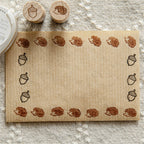 Hedgehog and acorn wooden stamps with repeated impressions forming border on kraft paper.