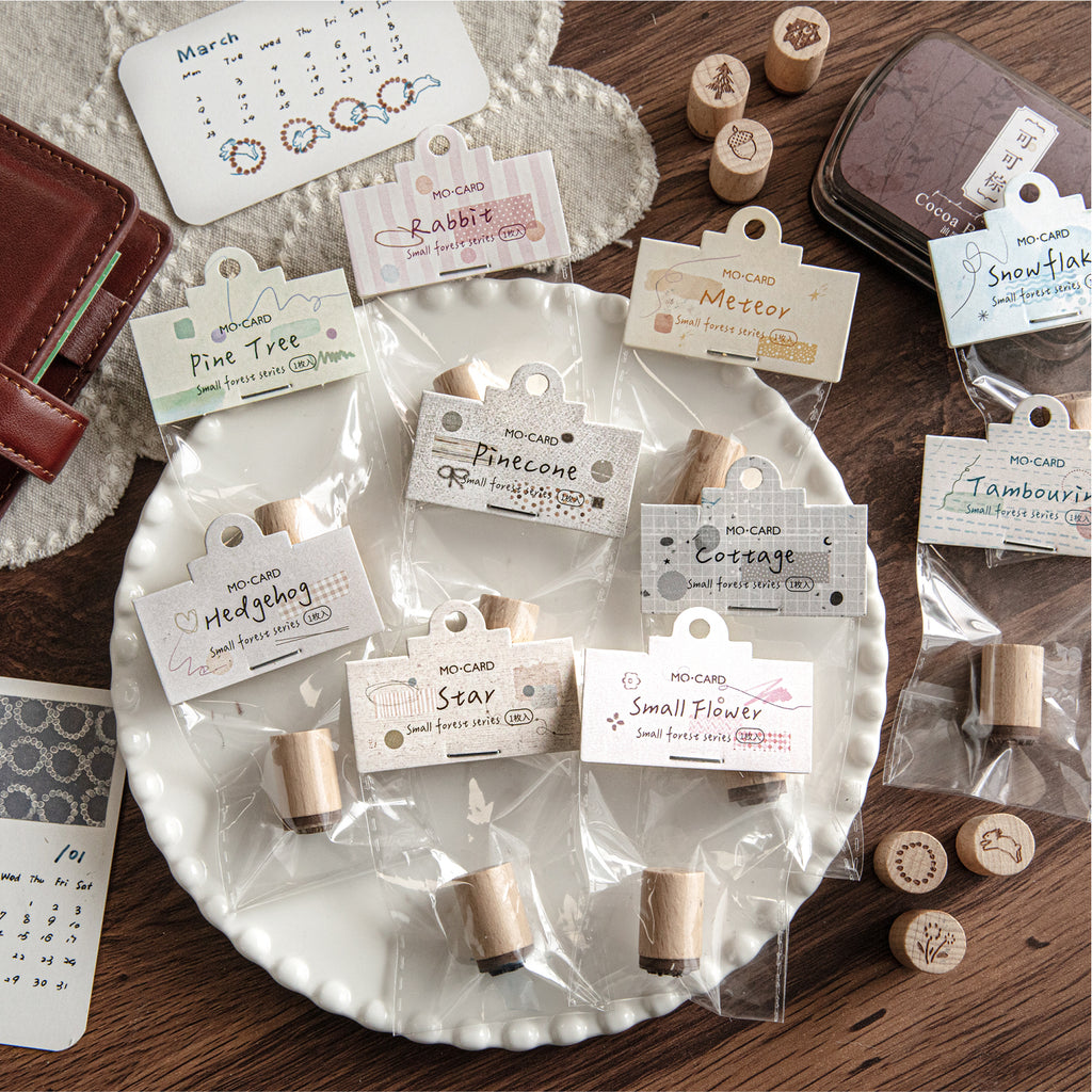 Ten forest theme wooden stamps in clear bags with illustrated tags, arranged on white ceramic tray.