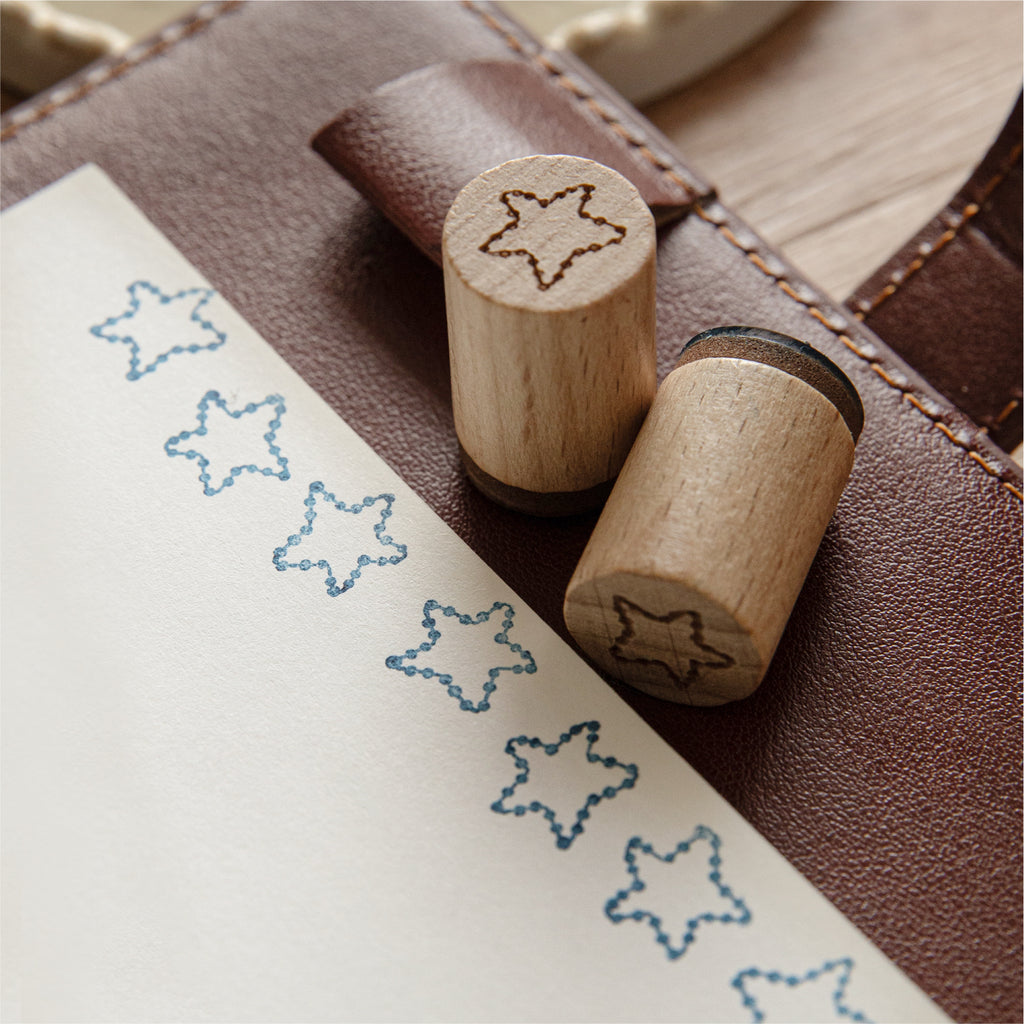 Pine tree and shooting star wooden stamps beside stamped journal cards on textured fabric background.