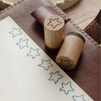 Pine tree and shooting star wooden stamps beside stamped journal cards on textured fabric background.