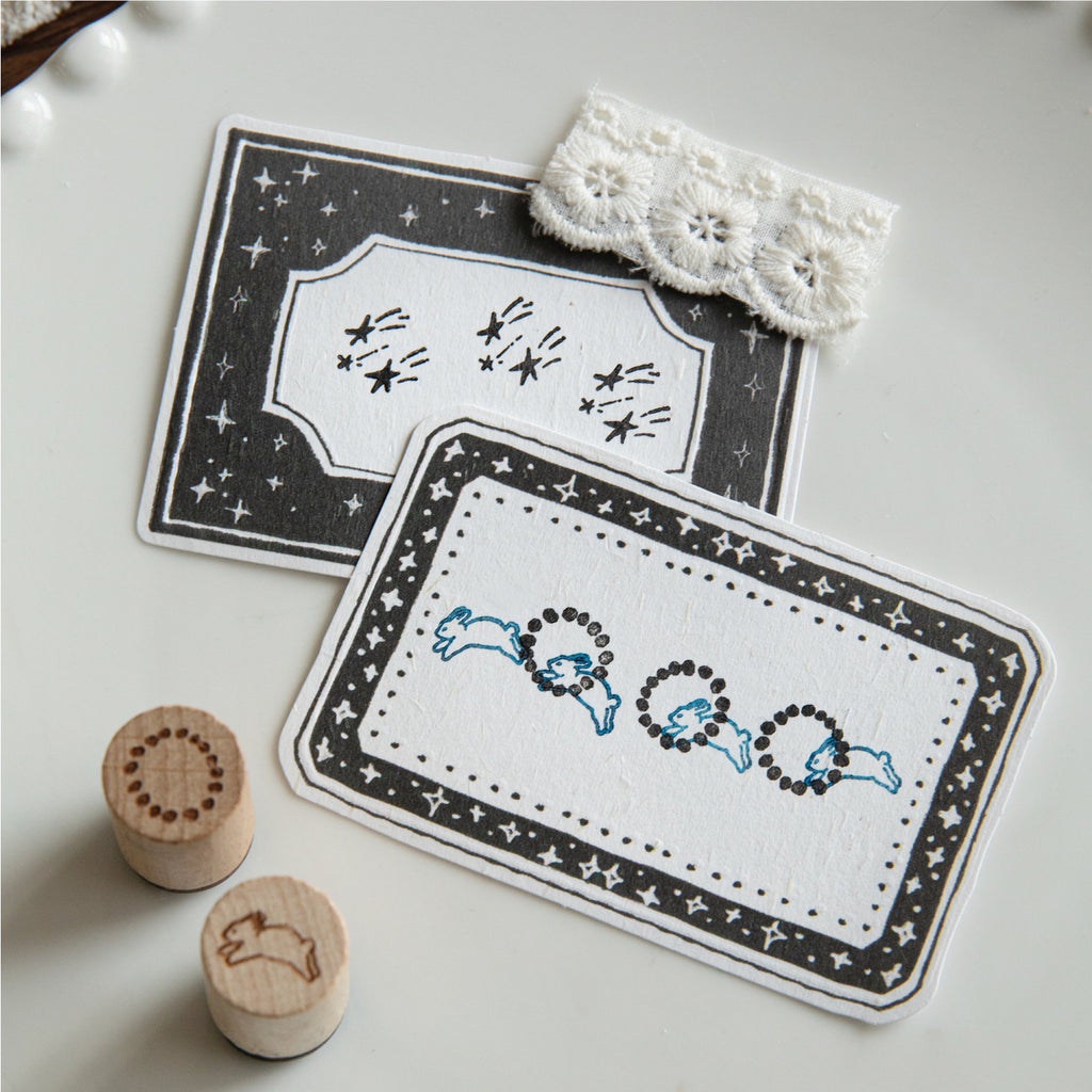 Rabbit and meteor wooden stamps with impressions on star-bordered journal cards, white lace detail.