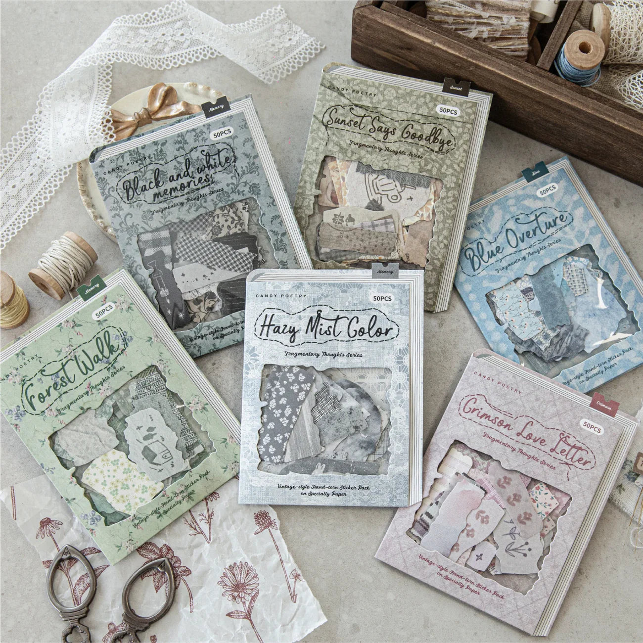 A beautiful flat lay showcasing all 6 styles of the Fragmentary Thoughts faux-fabric scrap sticker packs, surrounded by vintage crafting props like lace, spools of thread, and antique scissors.