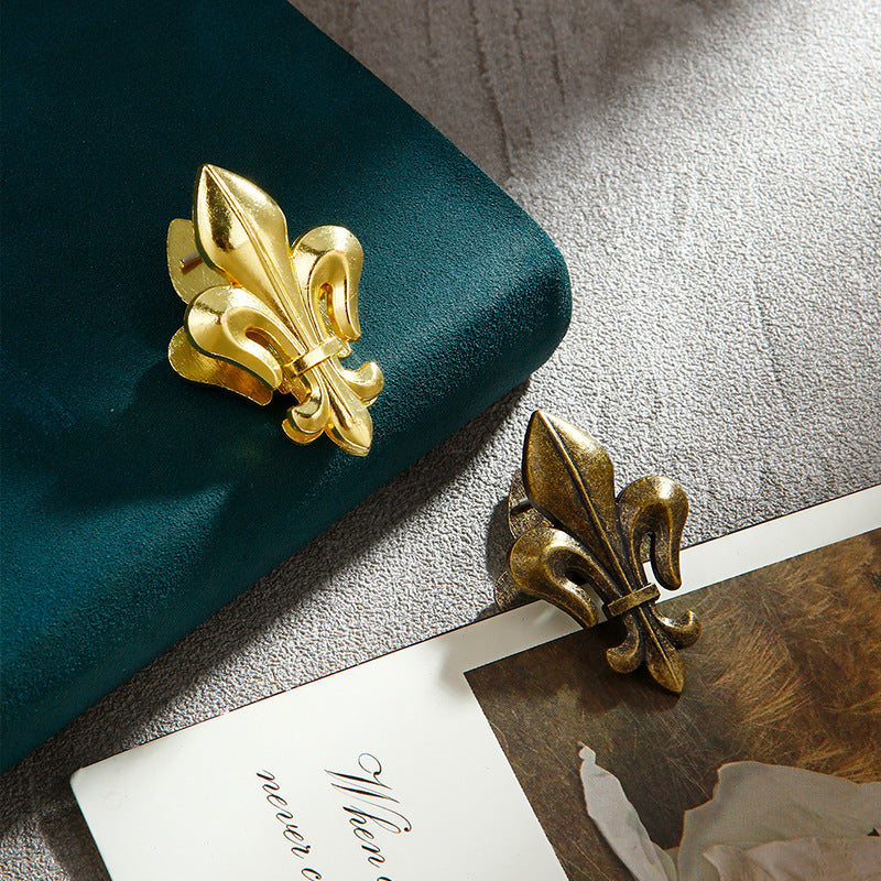 A comparison shot showing the two color options of Fleur-de-lis metal journal clips: Luminous Gold and Aged Antique Bronze. Highlights the classical gold aesthetics and textured vintage bronze style.