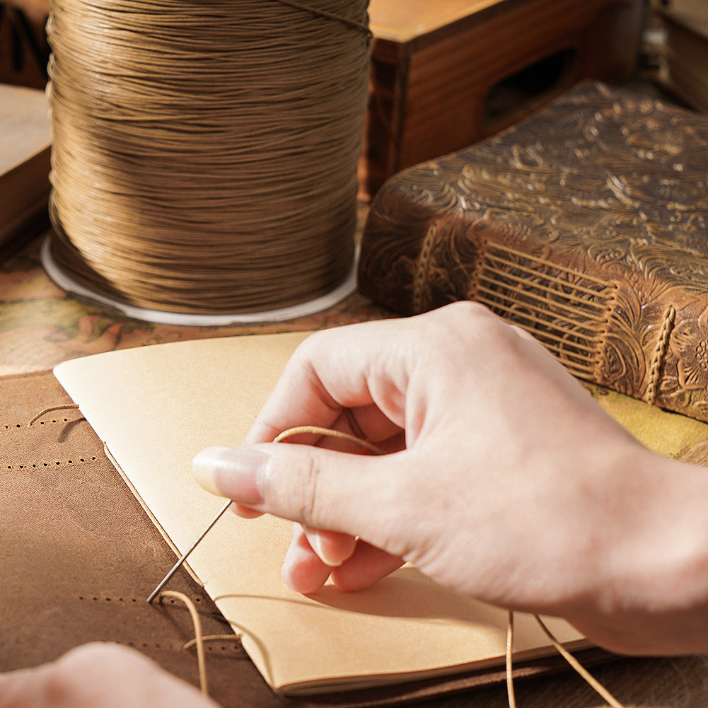 Artisan hand-stitching a leather sketchbook spine with waxed thread