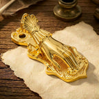 A luminous gold Victorian Lady's Hand metal journal clip clamping aged paper with typed text, on a soft blurred background of vintage ephemera.