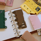 Close-up of brown portable 6-hole punch gripping white paper, showing alignment ruler and compact design.