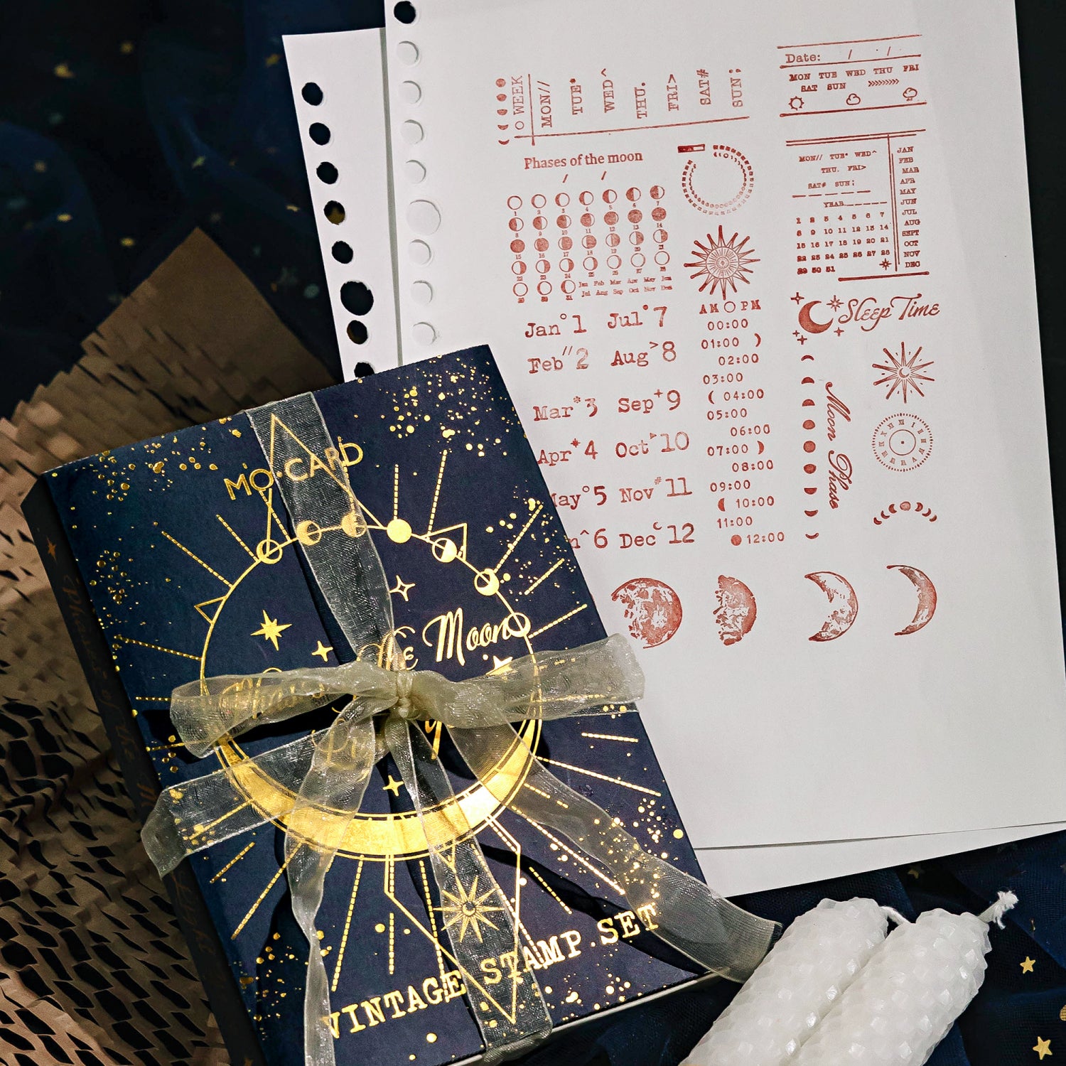 A sheet of paper displaying crisp red ink impressions of the moon phase and calendar stamps, placed next to the celestial navy blue gift box tied with an elegant ribbon for witchy gifting.