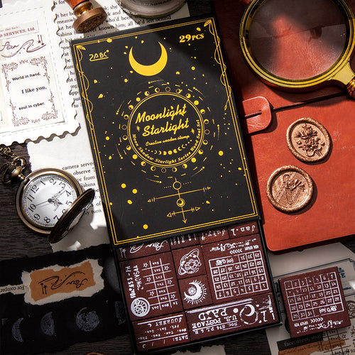 The Moonlight Starlight 29-piece vintage postal and celestial wooden stamp set in its elegant black and gold-foil box. Styled with a vintage pocket watch, magnifying glass, and wax seals for a dark academia aesthetic.