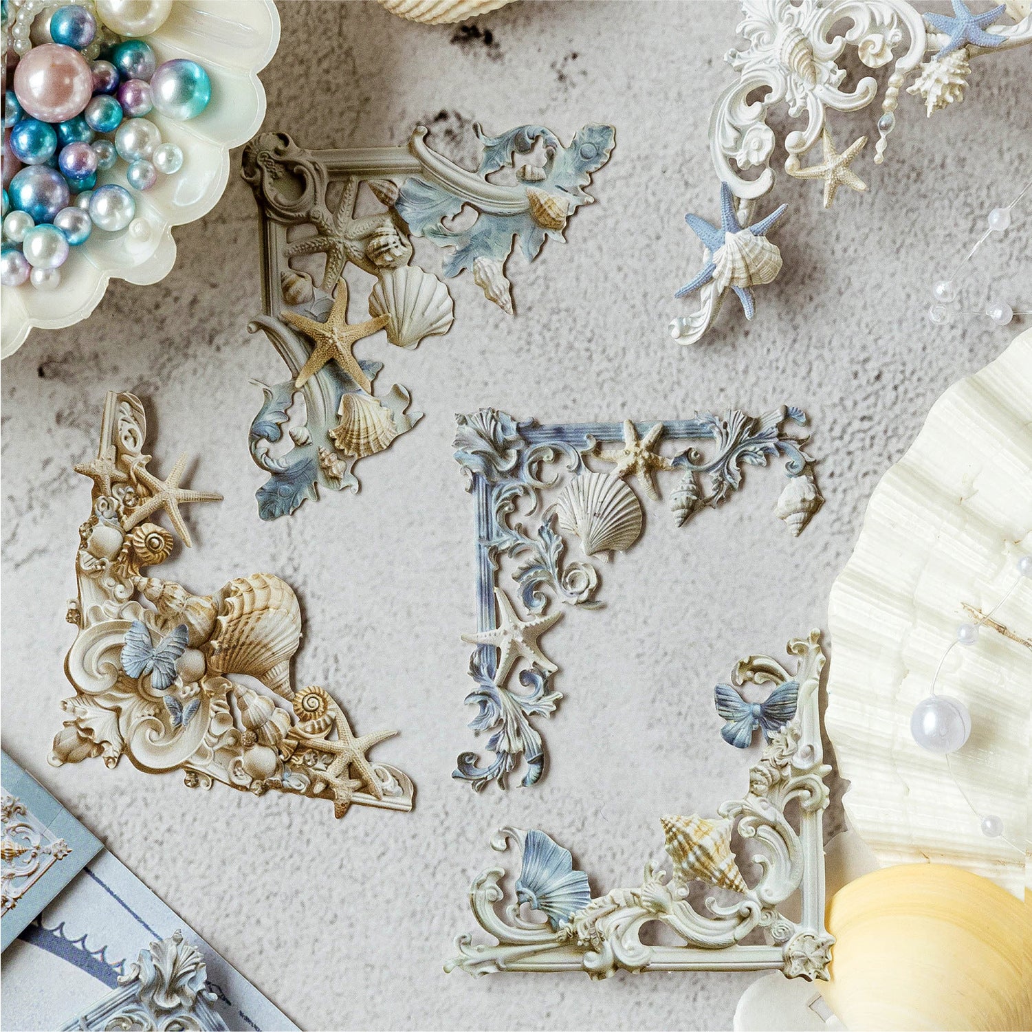 Close-up of the Oceanic Relics style 3D relief corner frame ephemera. Features laser-cut ocean blue pieces with starfish and seashell motifs, beautifully styled with scattered pearls and real shells.