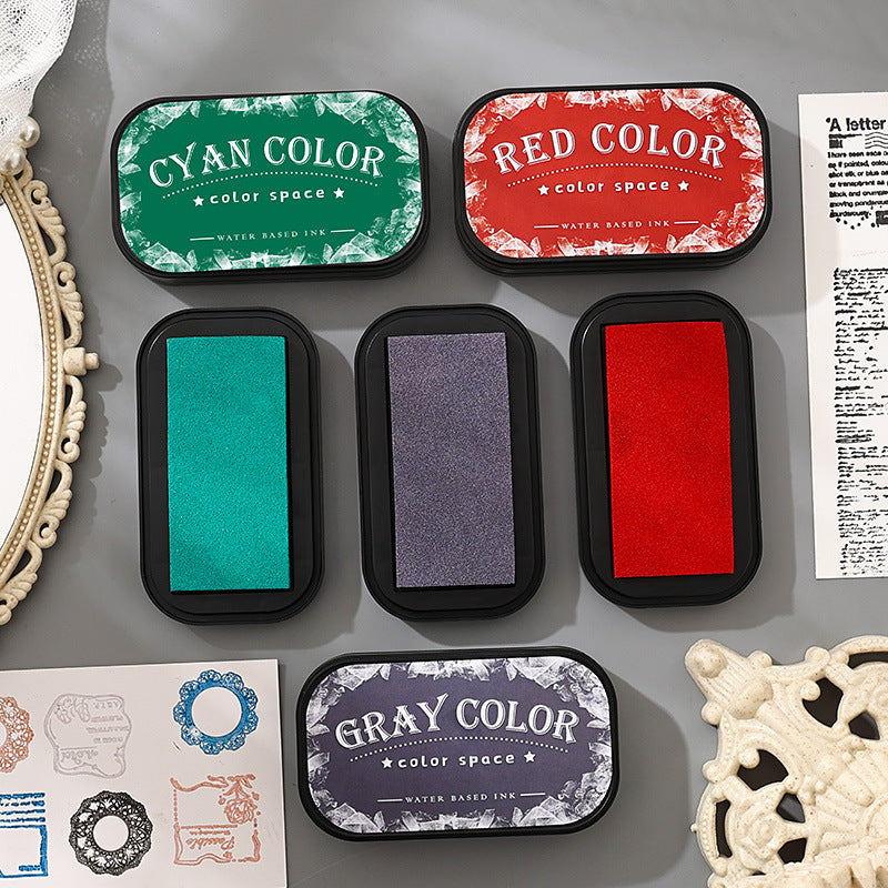 Open water-based ink pads in cyan, red, black and purple beside a kraft journal