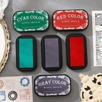 Open water-based ink pads in cyan, red, black and purple beside a kraft journal