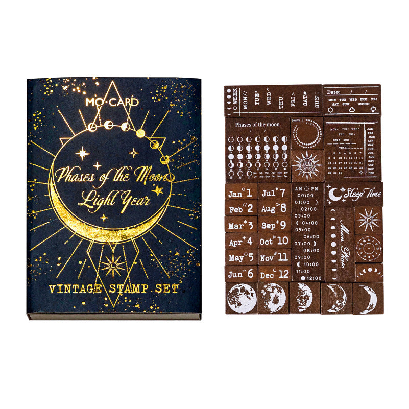 Clean studio shot of the complete Phases of the Moon celestial stamp set. Shows the luxurious navy and gold-foil matchbox packaging next to the neatly arranged 29 solid wood journaling stamps on a white background.