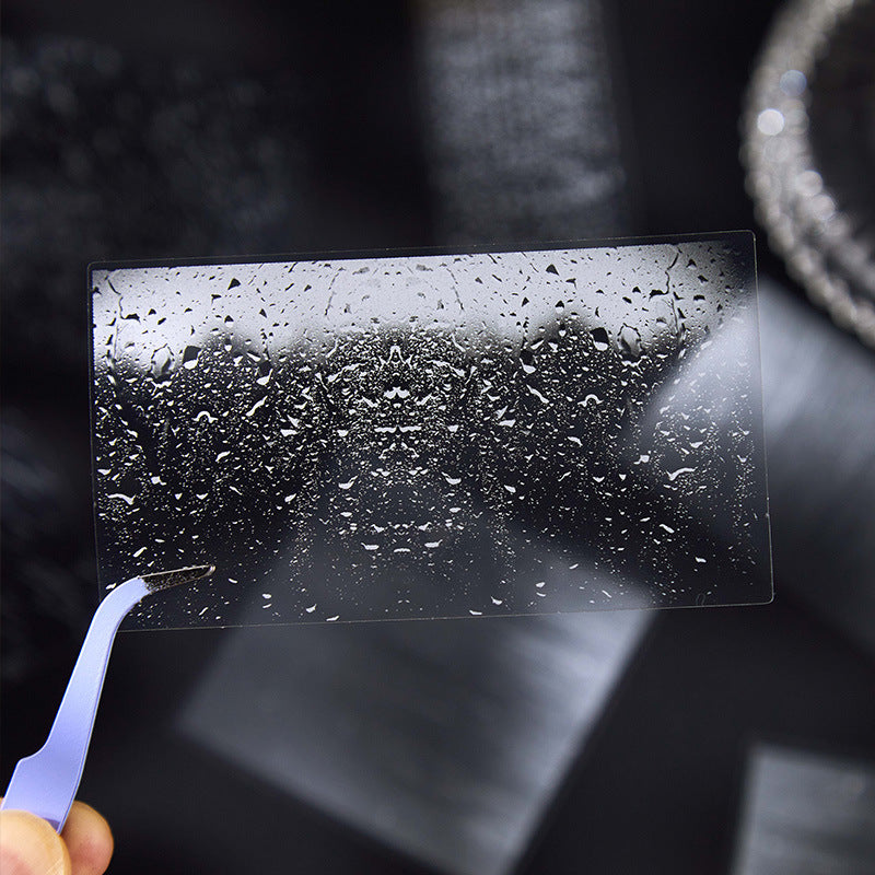 Single raindrop glass texture PET transparent sticker held by tweezers showing crystal-clear film detail for journal decoration