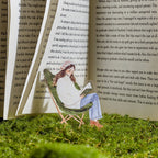 Green reading girl PET sticker clipped between open book pages on moss grass