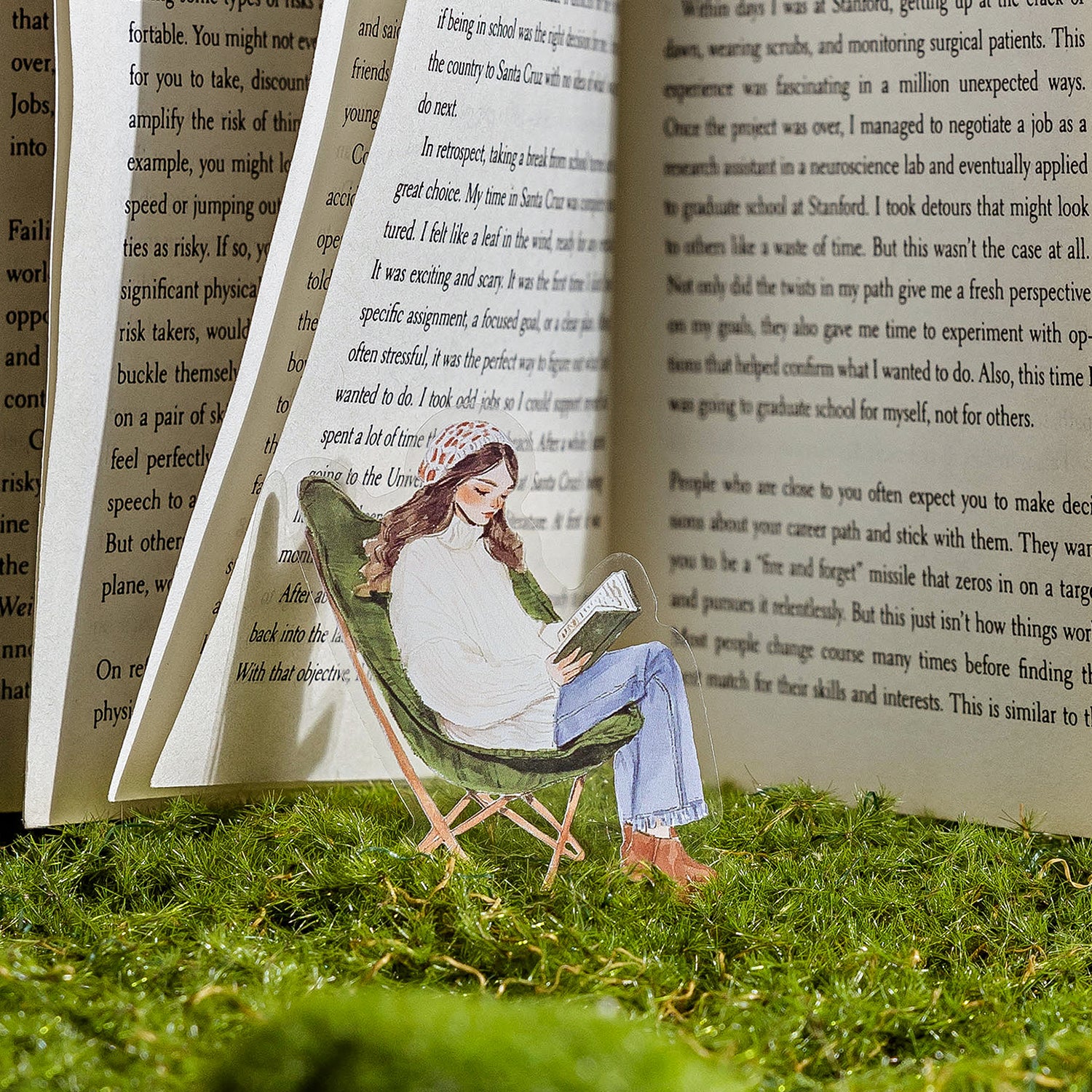 Green reading girl PET sticker clipped between open book pages on moss grass