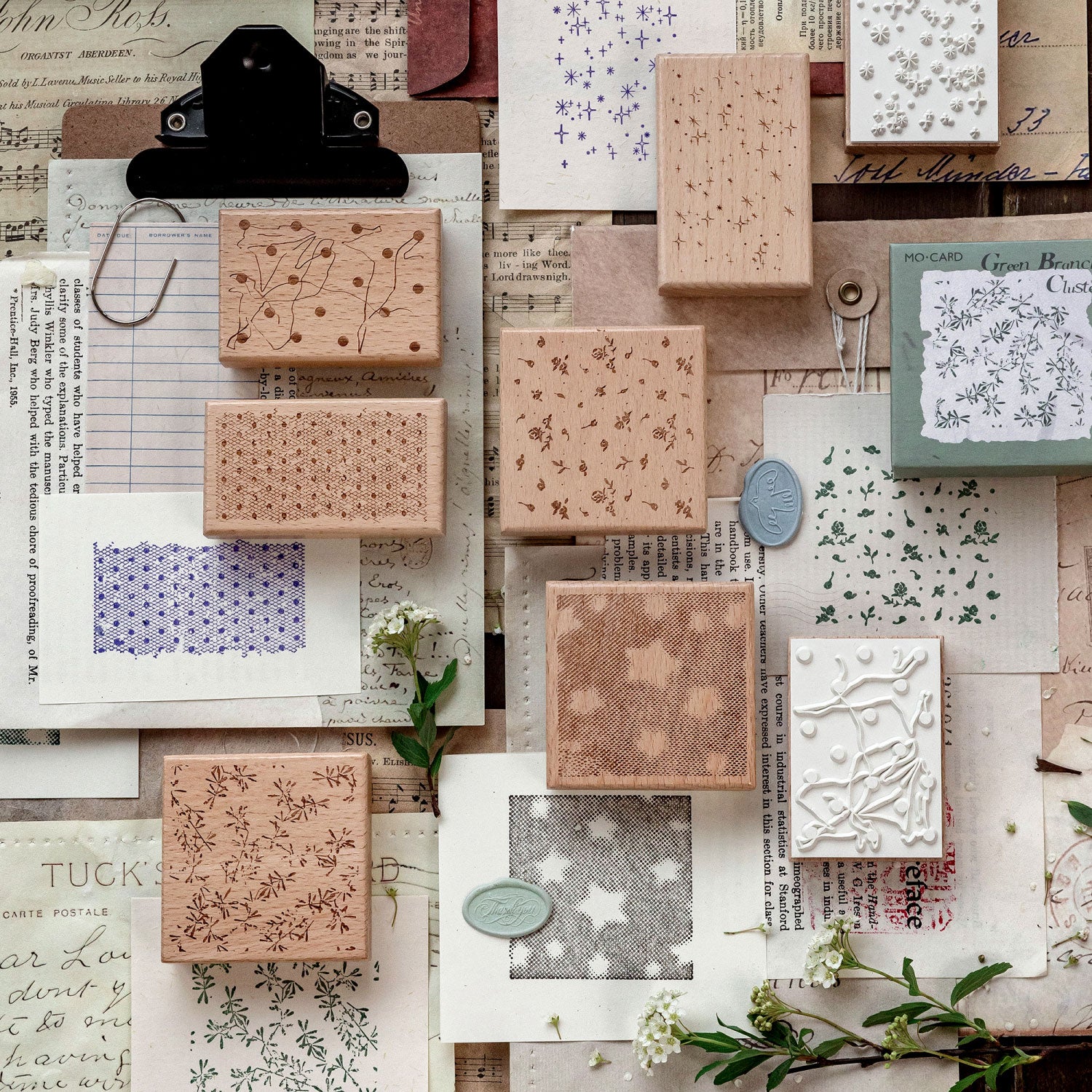 Multiple romantic background stamps with floral and star impressions on layered collage paper, wax seal and dried flowers.