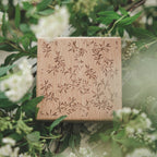 Floral print romantic background wooden stamp in fresh green foliage, soft botanical setting with natural light.