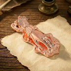 A beautiful and delicate romantic rose gold metal journal clip in the form of a Victorian Lady's Hand (no pearl detail). The warm pinkish-gold finish is polished and elegant. It is clamping down very old, worn paper with script, surrounded by soft dried rose petals, offering a beautiful cottagecore and vintage aesthetic.