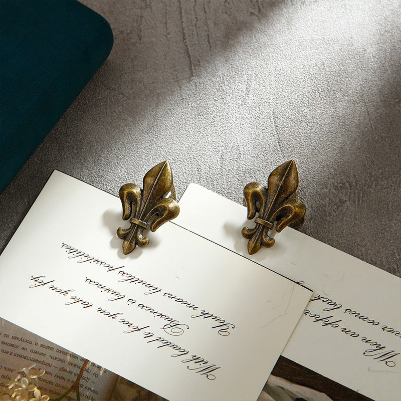 A matching set of two Aged Antique Bronze Fleur-de-lis metal binder clips securing thick, aged book pages. Emphasizing the detailed, textured heraldic design.