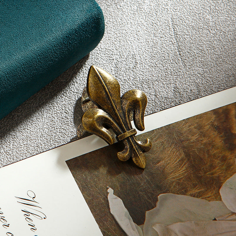 A single unit of the Aged Antique Bronze Fleur-de-lis vintage metal journal clip clamping onto aged script paper. Set in a classic Dark Academia composition.